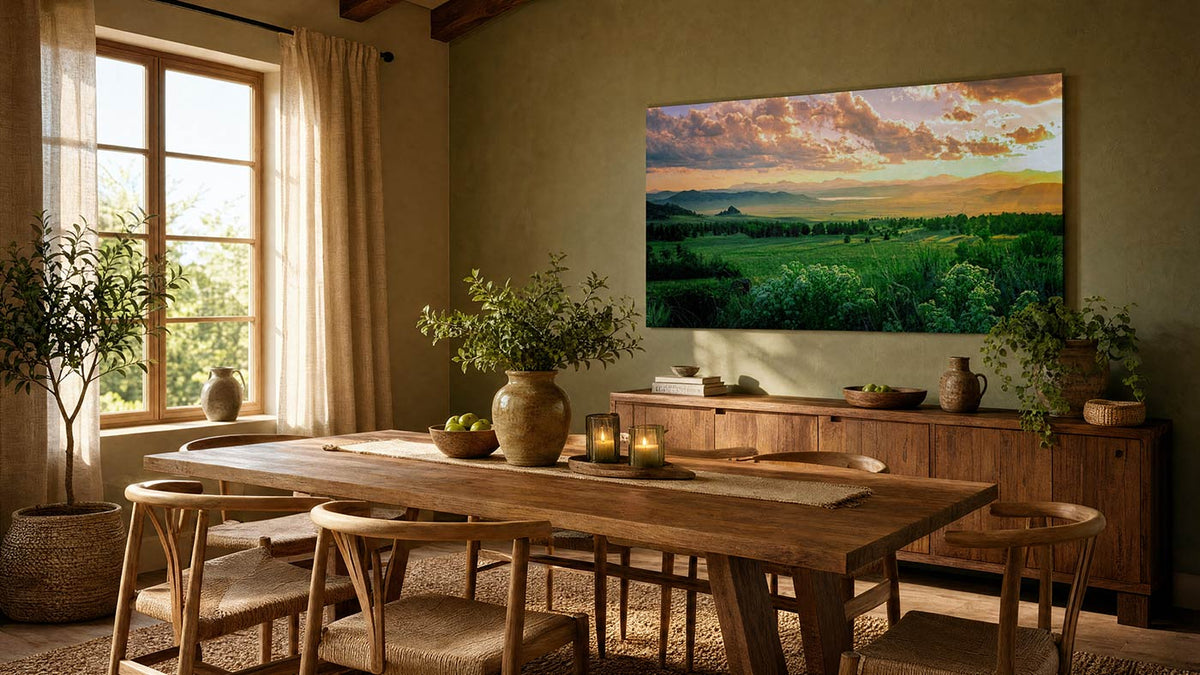 A large rectangular wall art print depicting a lush green landscape under a dramatic sunset sky, displayed in a warm, rustic dining room above a wooden credenza.