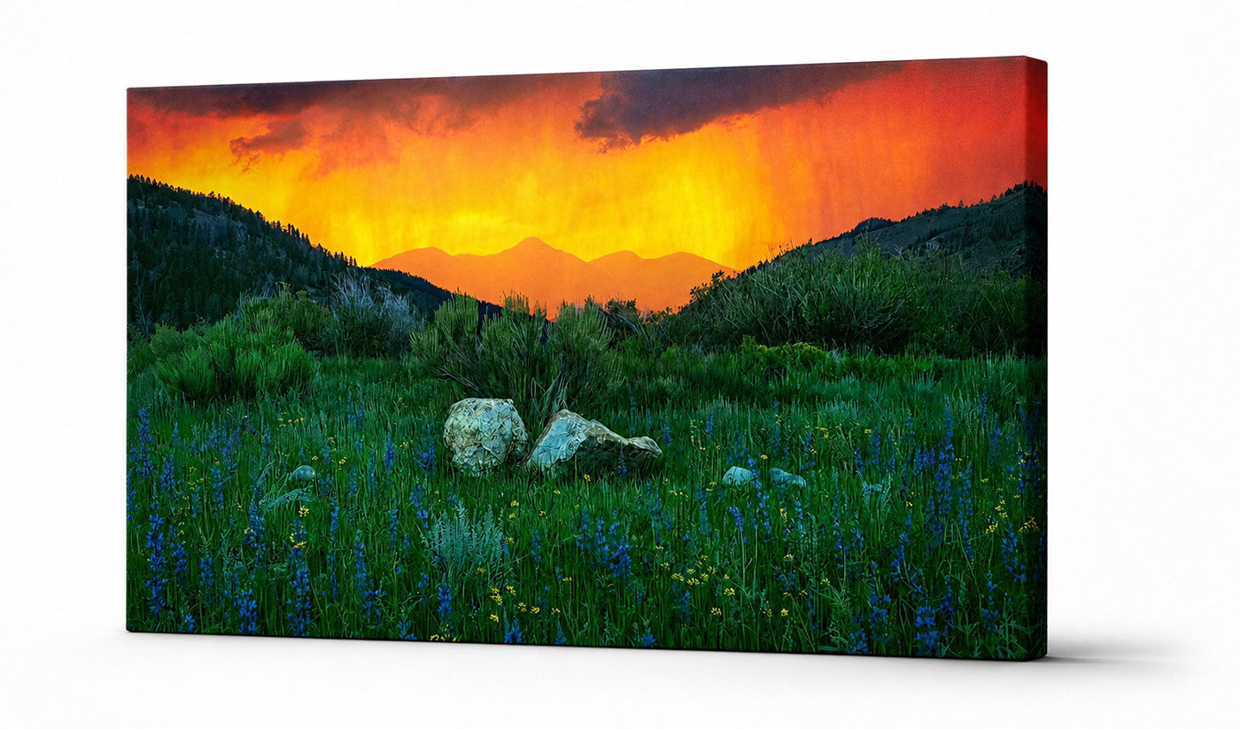Mountain sunset meadow wall art canvas print featuring a fiery orange sky, wildflowers, and distant peaks